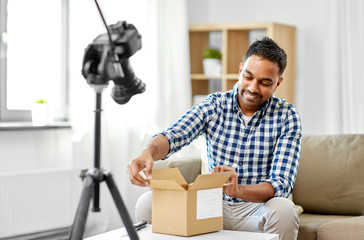 mail delivery, shipment and blogging concept - happy indian male blogger opening parcel box and recording unboxing video with camera at home