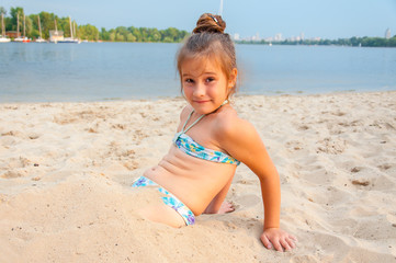 Girl playing with sand on the beach. Girl in a swimsuit molds of sand near the sea