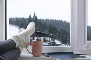 Woman with cup of winter drink and notebook near window, closeup