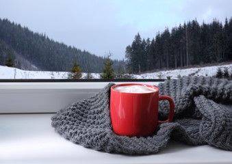 Obraz na płótnie Canvas Hot drink and warm scarf near window with view of winter mountain landscape
