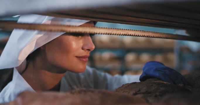 Closeup perfect look of young woman baker in a bakery she smelling excited the fresh baked bread and take some from the industrial shelf