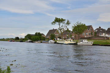 Obraz premium Kanał żeglowny z łódkami przy brzegu wśród drzew i domów mieszkalnych.