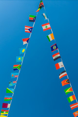 Colorful paper flags of different countries hanging on wires, blue sky in the background. International travel concept.