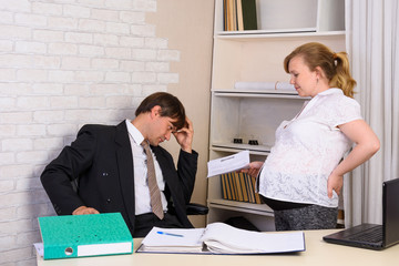 A pregnant office employee stands next to the table and shows the contract, the boss looks thoughtfully into the document.
