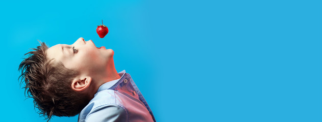 red strawberry berry falls to a boy in a blue shirt right in his mouth on light background