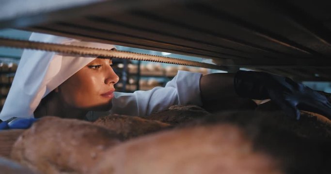 Good looking lady baker in a stylish uniform in a bakery kitchen put in order the fresh baked bread after she take some bread from shelf smelling with pleasure and go. shot on red epic