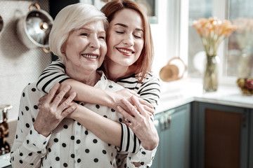Young woman smiling while kindly hugging her aged mother