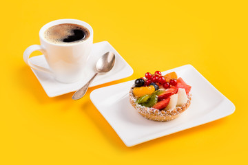 A cupcake with fruit and a cup of coffee on a yellow background. Breakfast dessert