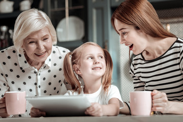 Little girl holding modern tablet and her mother looking excited