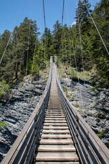 Fototapeta premium View of a wild river in a gorge with a modern suspension bridge with the name Traversinersteg, in the Swiss Alps