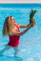 Young girl with blonde curly hair throw pineapple in air on the pool