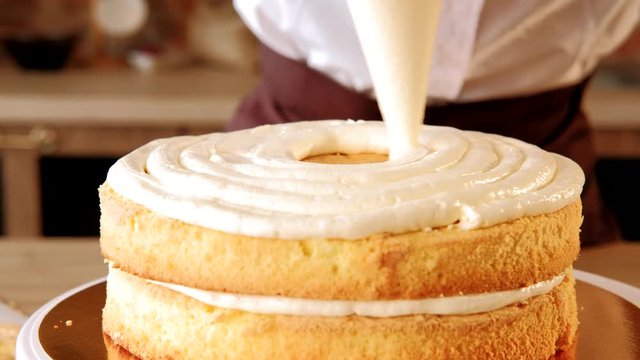 Cake recipe. Pastry chef piping out cream filling on to a sponge cake layer