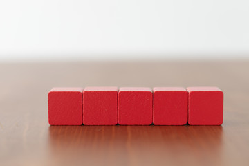 Five red wooden cubes in a row beside each other on wooden table woth copyspace on the front for lettering