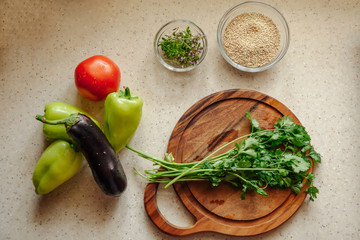 Fresh greenery on the cutting board. Eggplant, pepper and tomato lie next to a cutting board on the table.