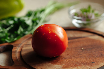 Fresh tomato lies on a cutting board against the background of fresh greens