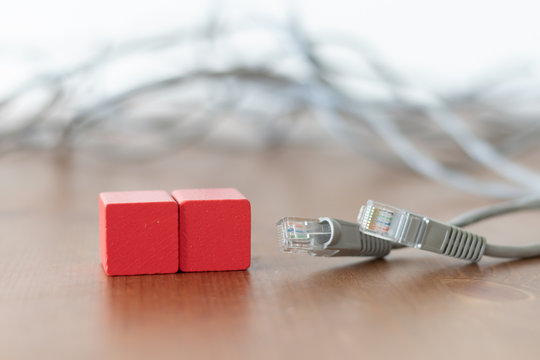 Two red wooden cubes with copyspace on the front beside grey lan cable on wooden table 