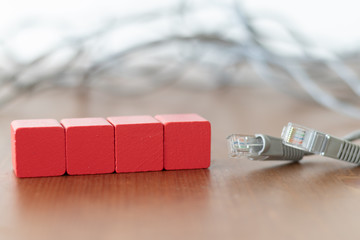 Four red wooden cubes with copyspace on the front beside grey lan cable on wooden table 