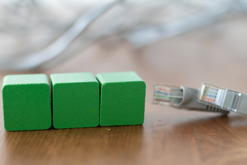Three green wooden blocks with copyspace on the front beside grey lan cable on wooden table 