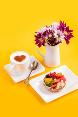 Breakfast. Cappuccino coffee, fruit cake and a bouquet of flowers on a yellow background. Congratulations on the holiday