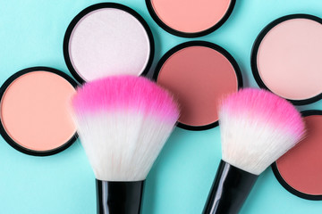 Bright coral blush on a trendy pastel blue background. Pink makeup brushes. Compact powder of different colors. Cosmetic products. Beauty salon concept. Closeup. For contouring. eye shadow
