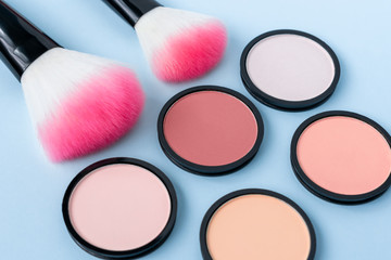 Obraz na płótnie Canvas Bright coral blush on a trendy pastel blue background. Pink makeup brushes. Compact face powder in different colors. Cosmetic products. Closeup. Corrector for contouring.