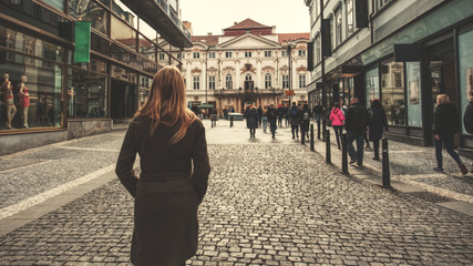 Back view of young girl in brown coat walking on a city street