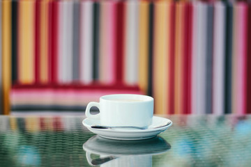 White cup of coffee with a saucer on the table close-up in an outdoor cafe on the street.