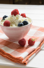 bowl of cottage cheese with raspberries and blueberriesand on the red plaid litter on a white wooden table
