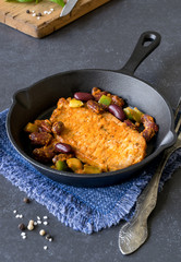 A cooked steak with vegetables in a cast iron frying pan on a dark stone background