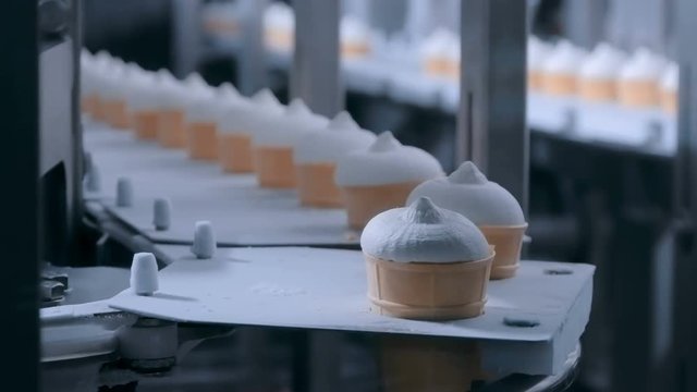 Dairy industry, manufacturing and automated technology equipment concept - conveyor belt with icecream cones at modern food processing factory - icecream automatic production line