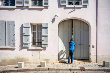 Fototapeta na wymiar Man in hat peers into the courtyard of the house with shutters through slightly open gate