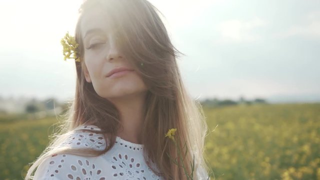 At sunlight attractive young woman stand in field feel freedom hold sniffs the flower blooming yellow field happy smile meadow green landscape sunlight model portrait close up slow motion
