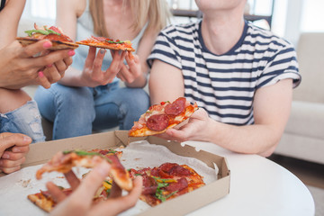 Young people eating pizza. Group of friends having lunch indoors. Funny friends together.