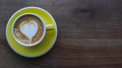 Macro photo cup of coffe cappucino in a yellow cup. Painted heart on skin coffe