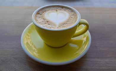 Macro photo cup of coffe cappucino in a yellow cup. Painted heart on skin coffe