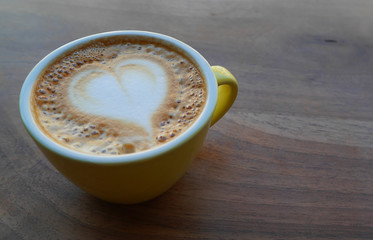 Macro photo cup of coffe cappucino in a yellow cup. Painted heart on skin coffe