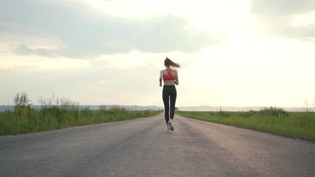 Shot back road runner woman running field sunset exercising outdoors fitness tracker wearable training marathon workout morning fitness adventure energy nature girl jogging healthy fit slow motion