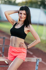 Portrait of young brunette woman athlete on stadium sporty lifestyle standing on track posing near the barriers running jumping to camera smiling playful