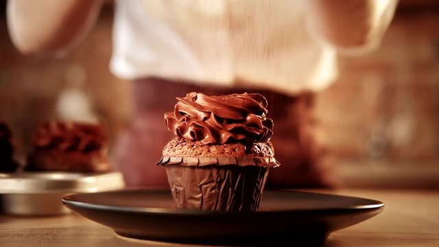 Chocolate cupcake perfection. Patisserie with whipped cream topping. Looped cocoa powder falling
