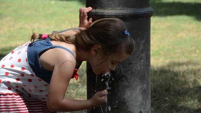 Little adorable baby girl drinks water from the drinking fountain of the roman nose on the streets of Rome