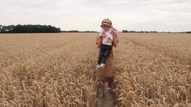 Young cute mother with curly child boy son hugging and spinning together walking in wheat field countryside nature