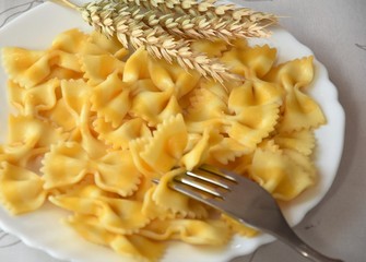 boiled pasta bows and ears of wheat on white tarlke with a fork