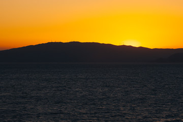 Sun setting behind the profile of an island carpeted with wind turbines