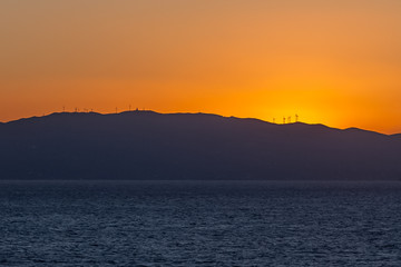 Sun setting behind the profile of an island with wind turbines