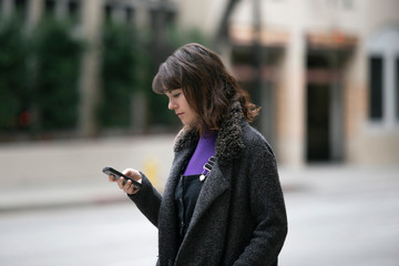 Young female using mobile phone app and waiting for a rideshare or pedestrian tourist checking...