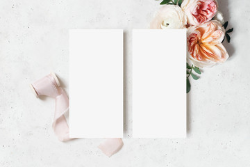 Wedding, birthday stationery mock-up scene. Blank menu cards. Decorative floral corner. Green leaves, pink English roses, ranunculus flowers and ribbon. Concrete table background. Flat lay, top view