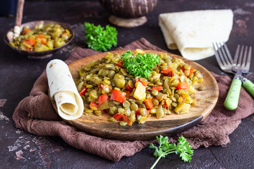 Green lentil stew (curry) with apple, bell pepper and onion. Selective focus. Dark stone background, rustic style.