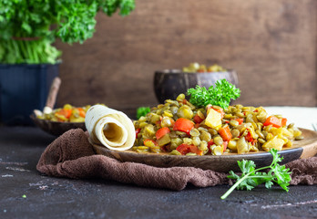 Green lentil stew (curry) with apple, bell pepper and onion. Selective focus. Dark stone background, rustic style.