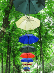 Umbrellas bright multi-colored hanging between the trees in the park