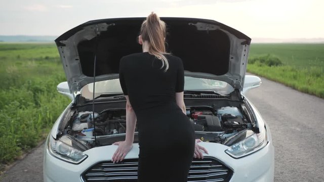 Shot back young woman looking at the engine of breakdown car at the field rural alone automobile girl help hood lost road trouble upset field repair side transportation travel slow motion